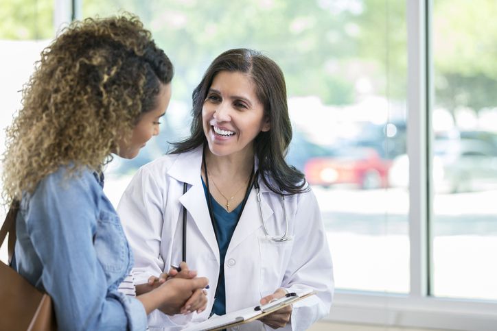 Caring mature female doctor shows test results to a young adult female patient. The doctor is smiling while talking with the patient.